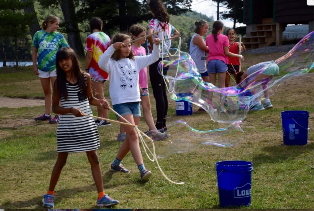 Large group of summer campers gathered outdoors playing with giant bubbles together